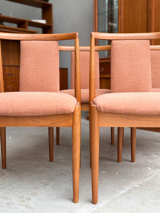 A set of four fully restored Parker T-Back Number 88 dining chairs in terracotta (Rediscover) is arranged on a gray floor, with wooden cabinets and shelves in the background.