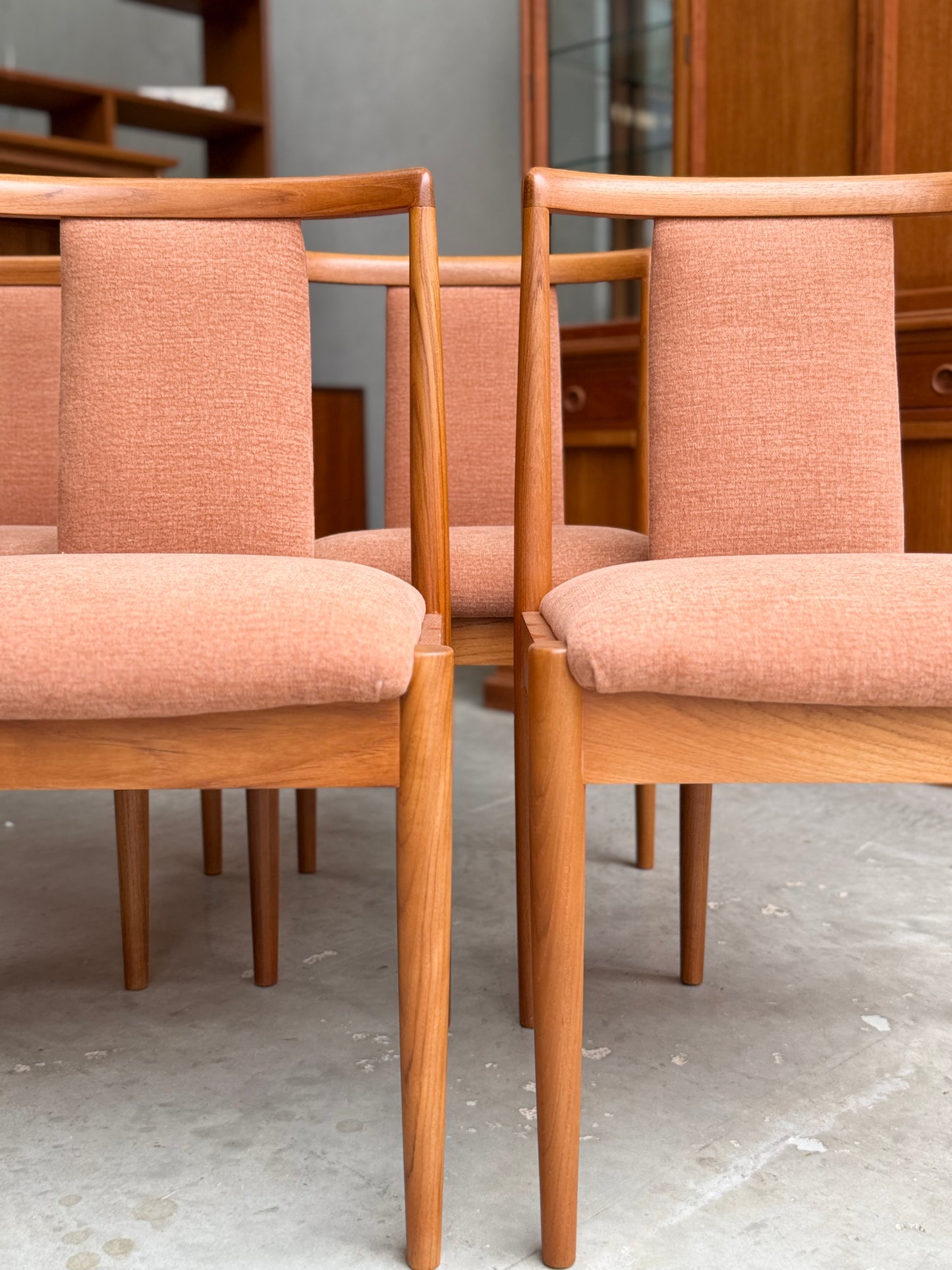 A set of four fully restored Parker T-Back Number 88 dining chairs in terracotta upholstery is arranged in pairs on a light concrete floor, with a wooden cabinet visible in the background.