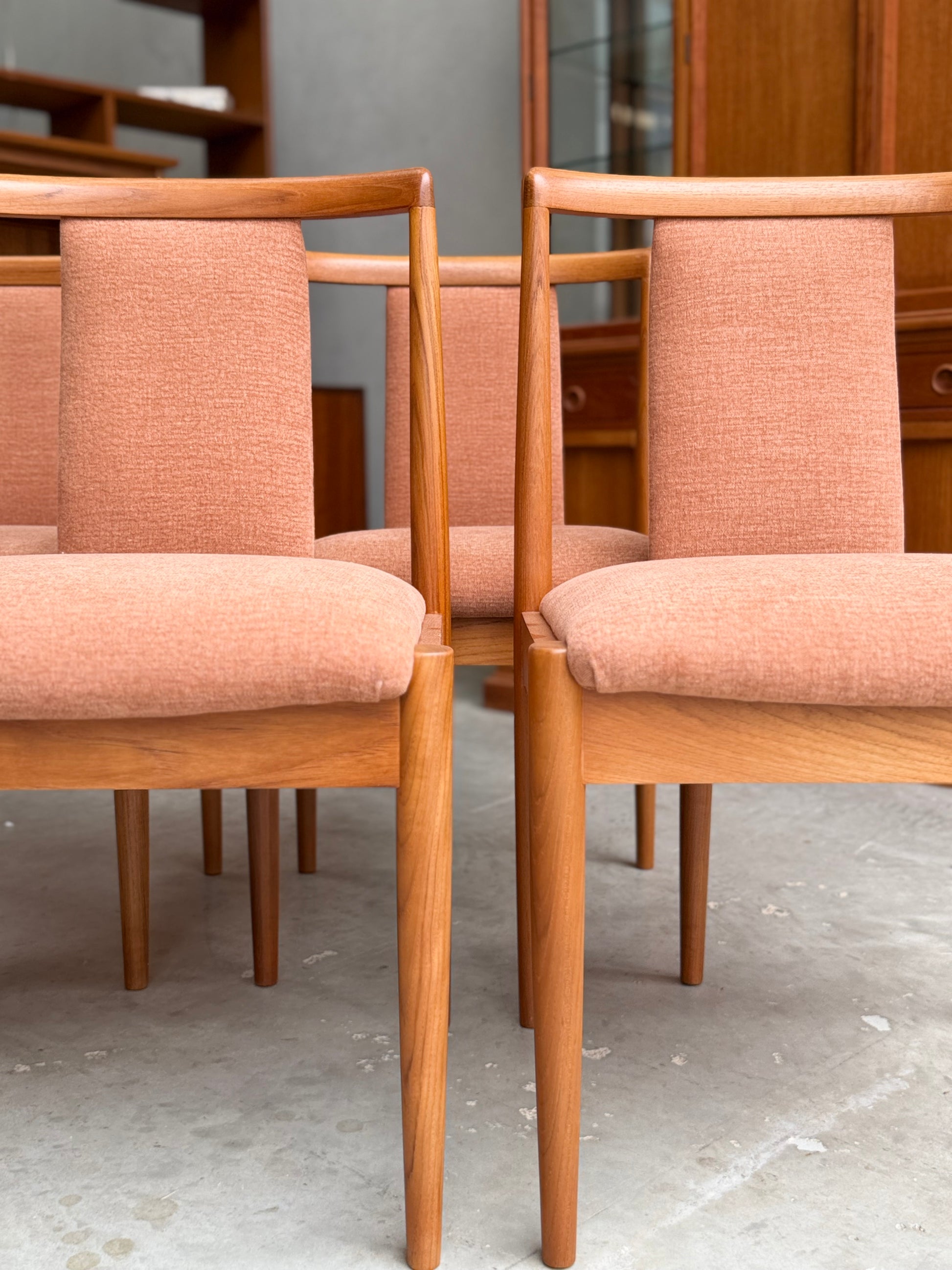 A set of four fully restored Parker T-Back Number 88 dining chairs in terracotta upholstery is arranged in pairs on a light concrete floor, with a wooden cabinet visible in the background.