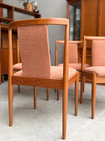 A close-up of the Fully Restored Parker T-Back Number 88 Dining Chairs Set of 4 - Terracotta by Rediscover, featuring light reddish-brown upholstery on a gray floor with wooden cabinets and shelves in the background.