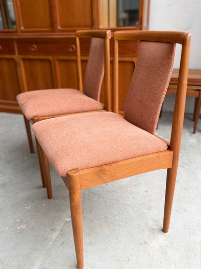Two fully restored Parker T-Back Number 88 dining chairs with terracotta upholstery are set side by side on a concrete floor, with a matching wooden cabinet in the background—classic mid-century modern style.