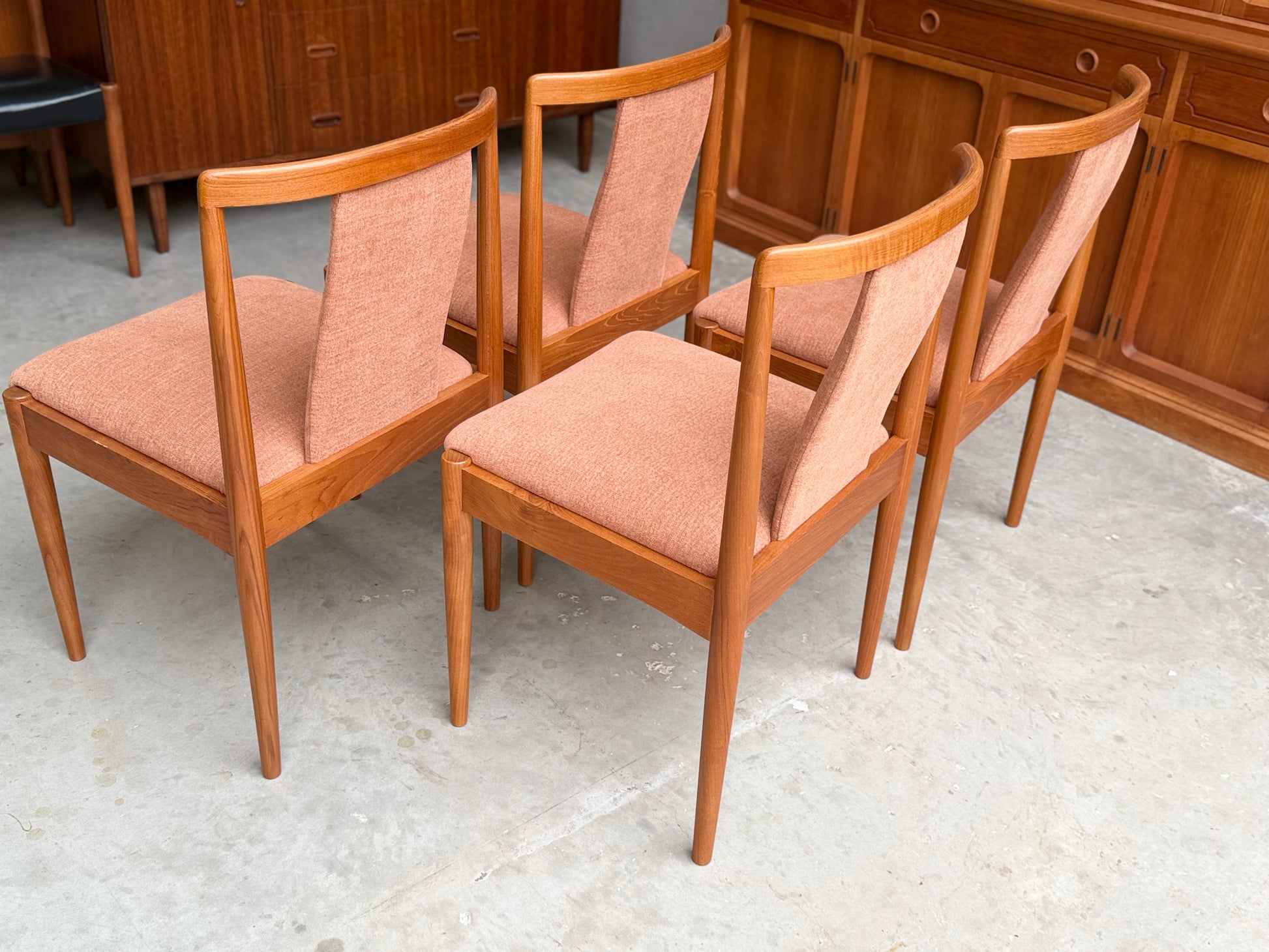 A set of four fully restored Parker T-Back Number 88 dining chairs in terracotta from Rediscover are arranged on a light concrete floor, with wooden cabinets in the background.