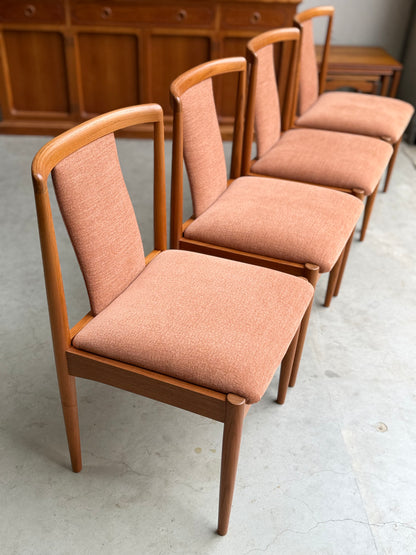 A set of four fully restored Parker T-Back Number 88 dining chairs in terracotta from Rediscover are arranged in a row on a light concrete floor, with a wooden sideboard visible in the background.