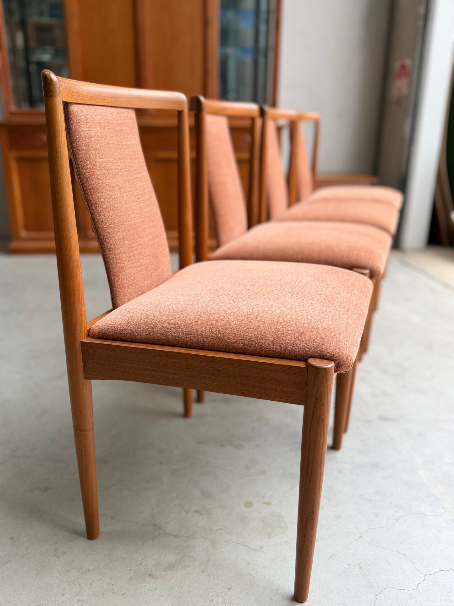 A set of four fully restored Parker T-Back Number 88 Dining Chairs in terracotta from (Rediscover), featuring wooden frames and neatly upholstered seats, arranged in a row on a light-colored floor in a bright indoor space.