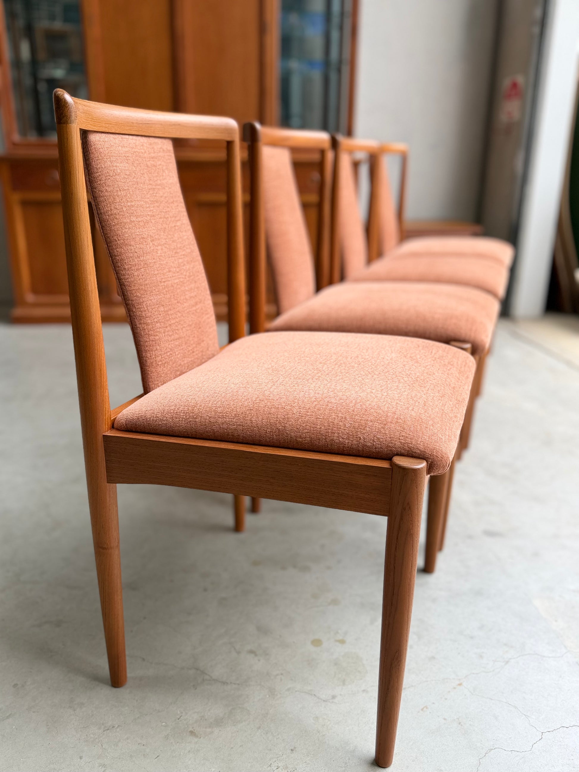 A set of four fully restored Parker T-Back Number 88 Dining Chairs in terracotta from (Rediscover), featuring wooden frames and neatly upholstered seats, arranged in a row on a light-colored floor in a bright indoor space.