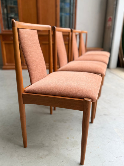 A set of four fully restored Parker T-Back Number 88 Dining Chairs in terracotta from (Rediscover), featuring wooden frames and neatly upholstered seats, arranged in a row on a light-colored floor in a bright indoor space.