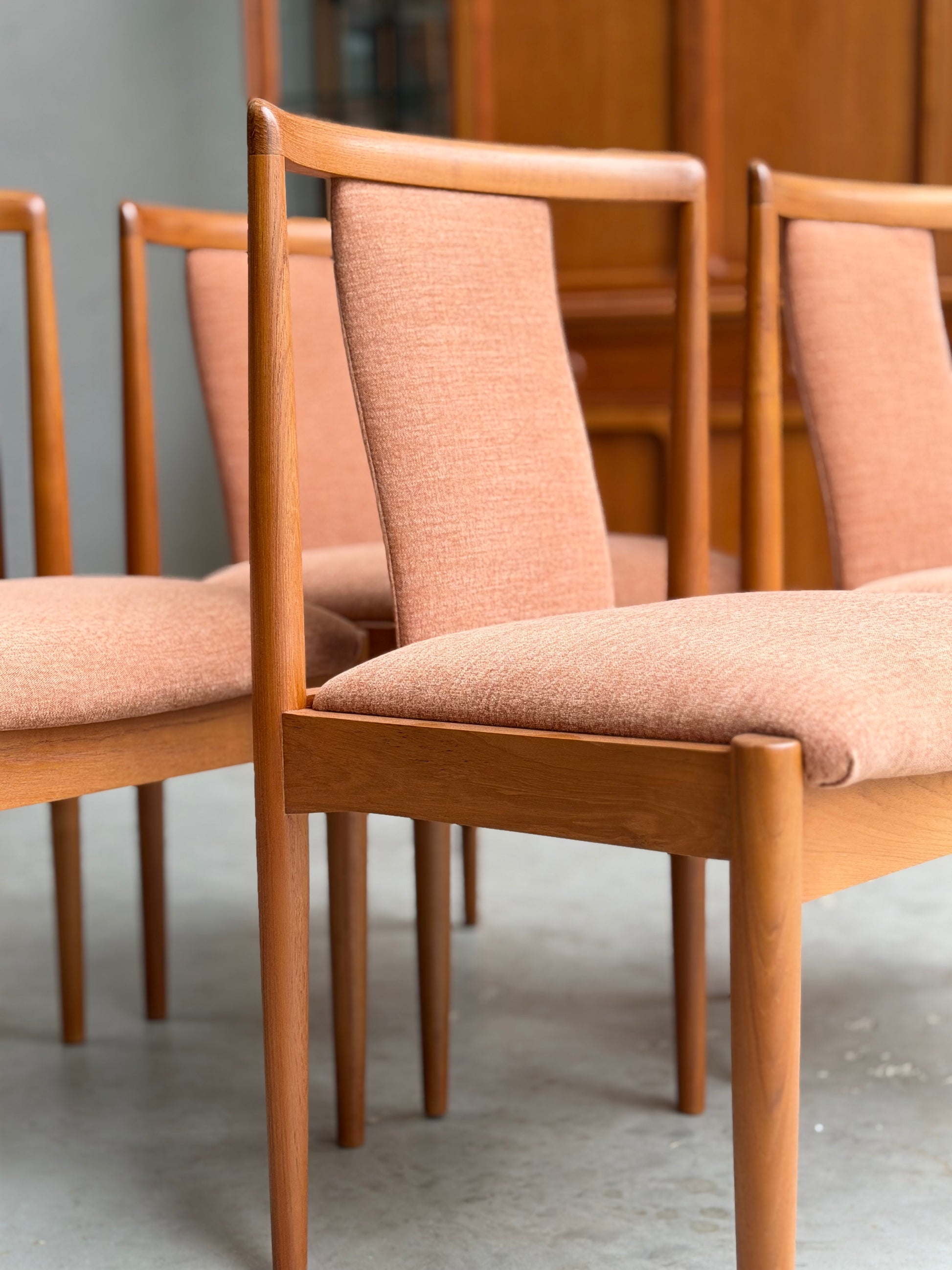 Four fully restored Parker T-Back Number 88 dining chairs in terracotta upholstery are arranged on a concrete floor, with wooden furniture visible in the background.