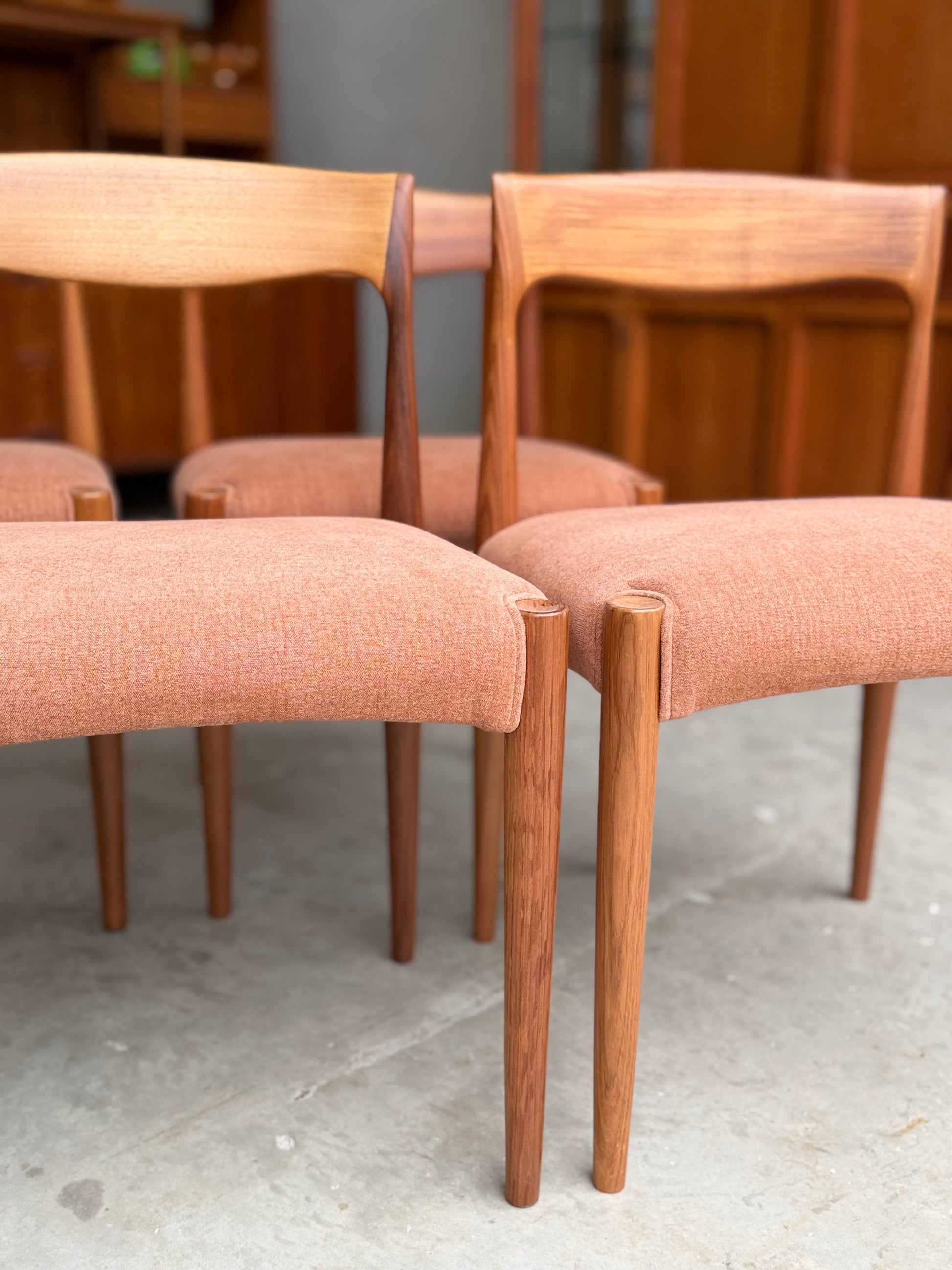 A set of four fully restored THB 'Milan' dining chairs (Rediscover) with curved backs and light brown seats are arranged together on a concrete floor, with wooden cabinets in the background.