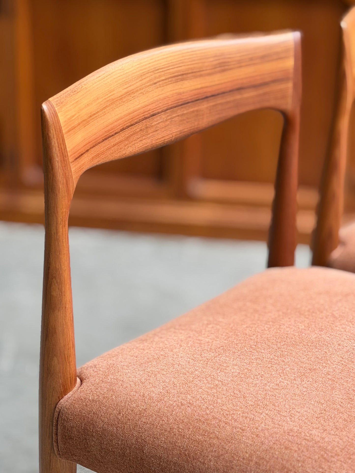 Close-up of a fully restored THB 'Milan' Dining Chair from the Rediscover set of 4, showcasing its curved backrest and light brown upholstered seat against blurred wood paneling and a gray floor.