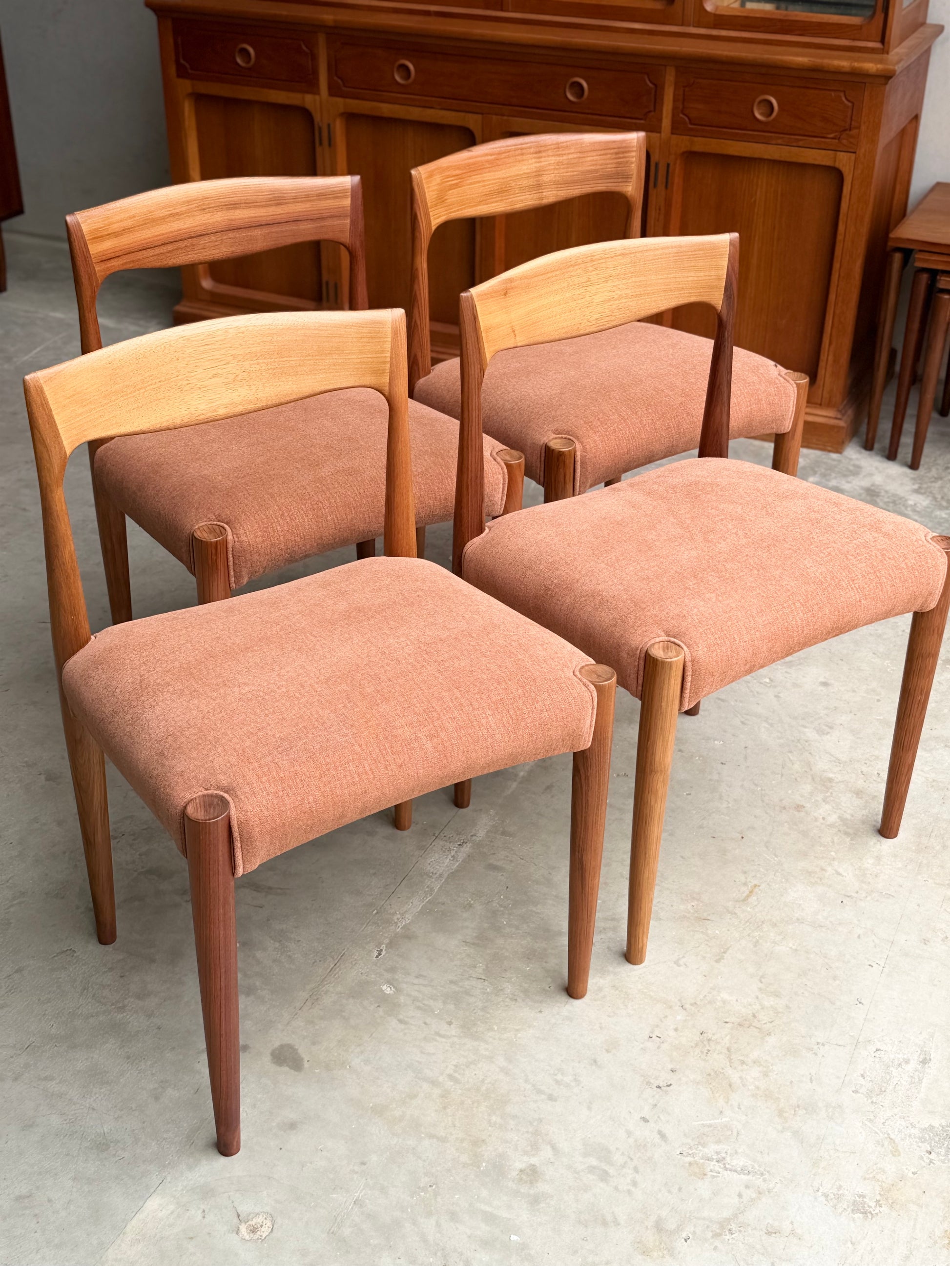 The Fully Restored THB 'Milan' Dining Chairs Set of 4 (Rediscover) features light brown wood frames and pinkish-tan upholstered seats, arranged on a concrete floor with other wood furniture in the background.