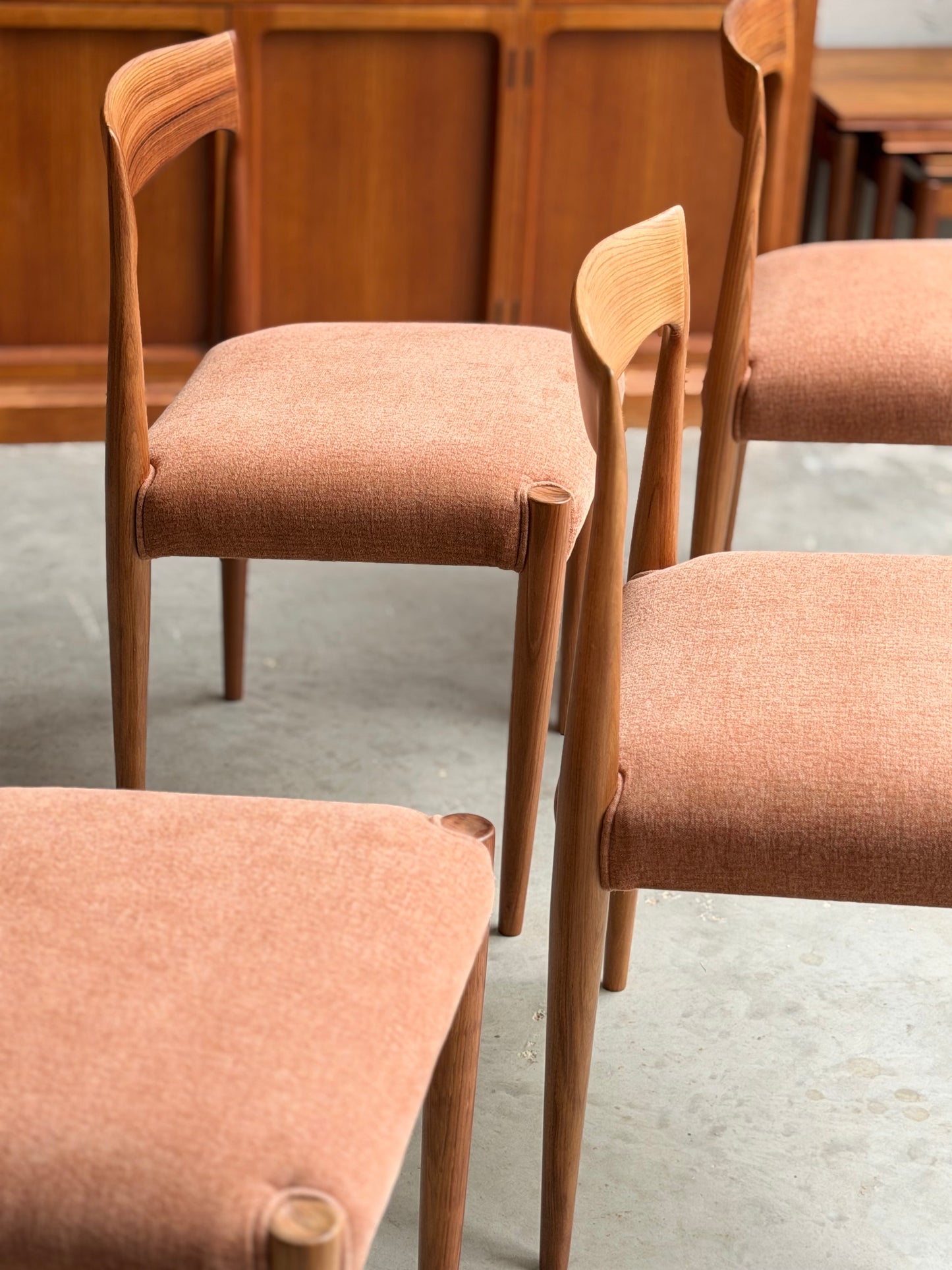 The Fully Restored THB 'Milan' Dining Chairs Set of 4 (Rediscover) feature light brown upholstered seats and backs, arranged on a concrete floor with a wooden cabinet behind, highlighting their timeless mid-century craftsmanship.