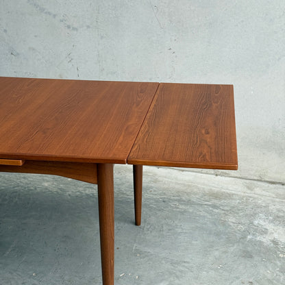 A close-up of the Fully Restored Parker 140 Square Extension Table (Rediscover) with a right drop-leaf extension, tapered legs, and a polished finish, set on a concrete floor against a plain gray wall for mid-century modern style.