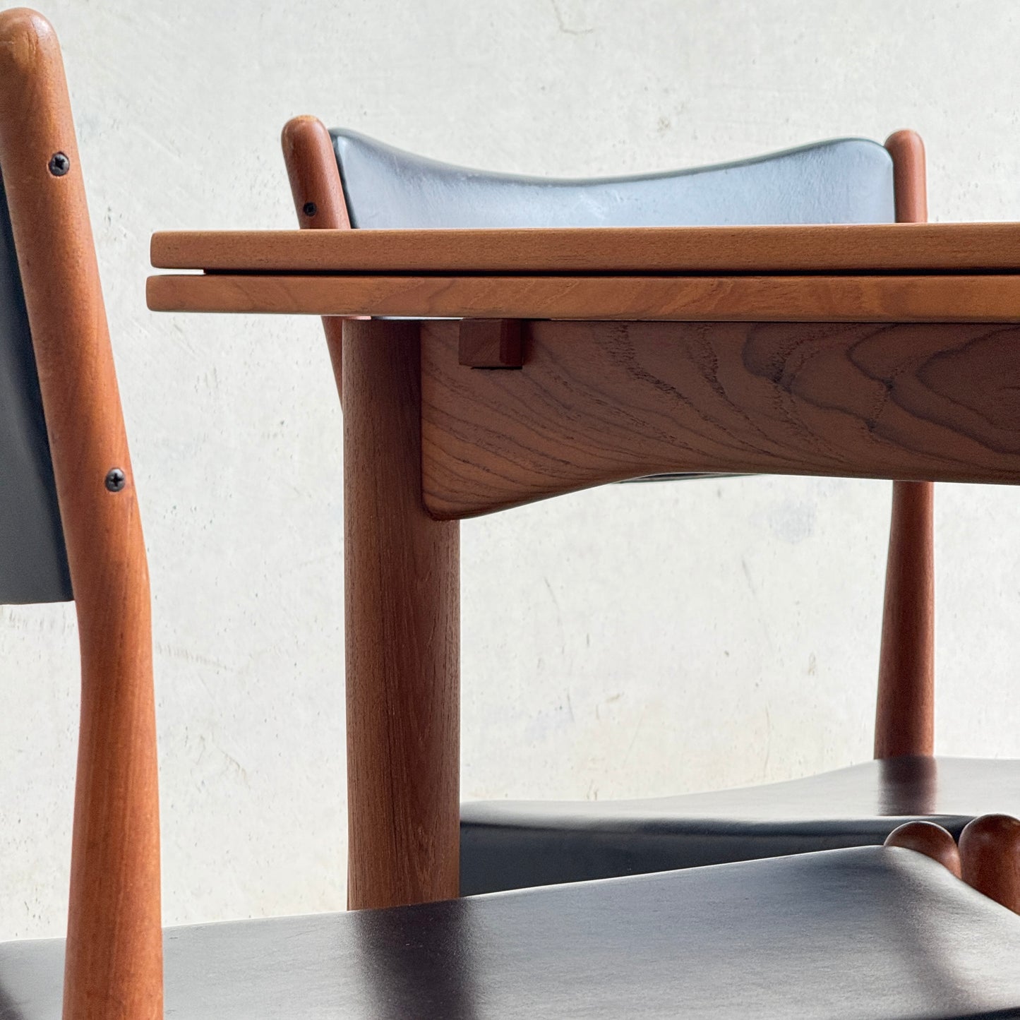 Close-up of the fully restored Parker 140 Square Extension Table (Rediscover) with two chairs featuring black seats and backrests, set against a light-colored wall for a timeless look.