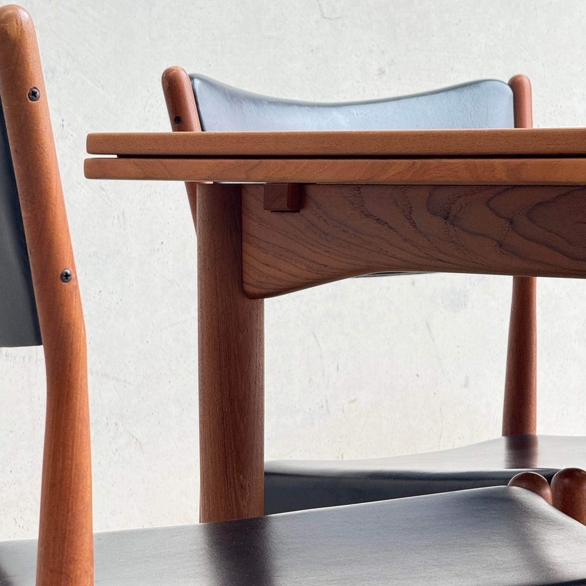 Close-up of the fully restored Parker 140 Square Extension Table (Rediscover) with two chairs featuring black seats and backrests, set against a light-colored wall for a timeless look.