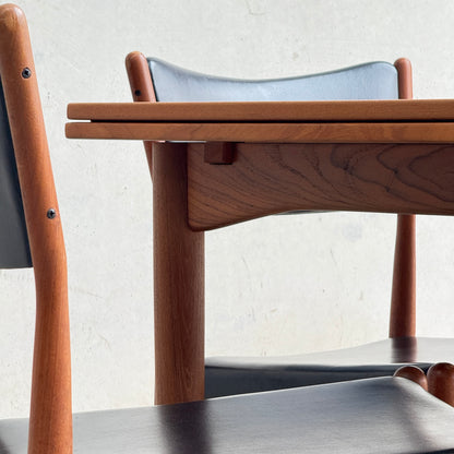 Close-up of the fully restored Parker 140 Square Extension Table (Rediscover) with two chairs featuring black seats and backrests, set against a light-colored wall for a timeless look.