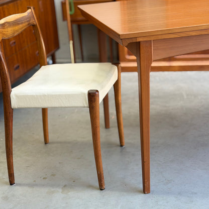 A wooden chair with a white cushion sits next to a Fler 64 Rectangular extension Table (Refine) on a gray concrete floor in a room with mid-century modern furniture.