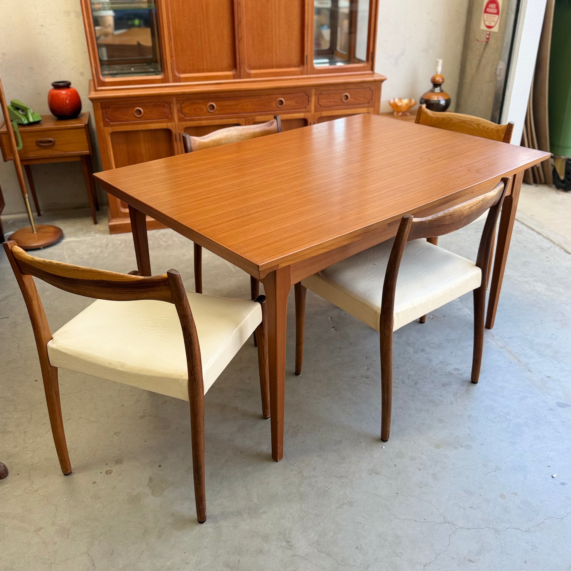 The Fler 64 Rectangular Extension Table (Refine) with four matching chairs featuring white cushions sits before a wooden cabinet on concrete floors, bringing vintage Australian mid-century modern charm to this eclectically decorated room.