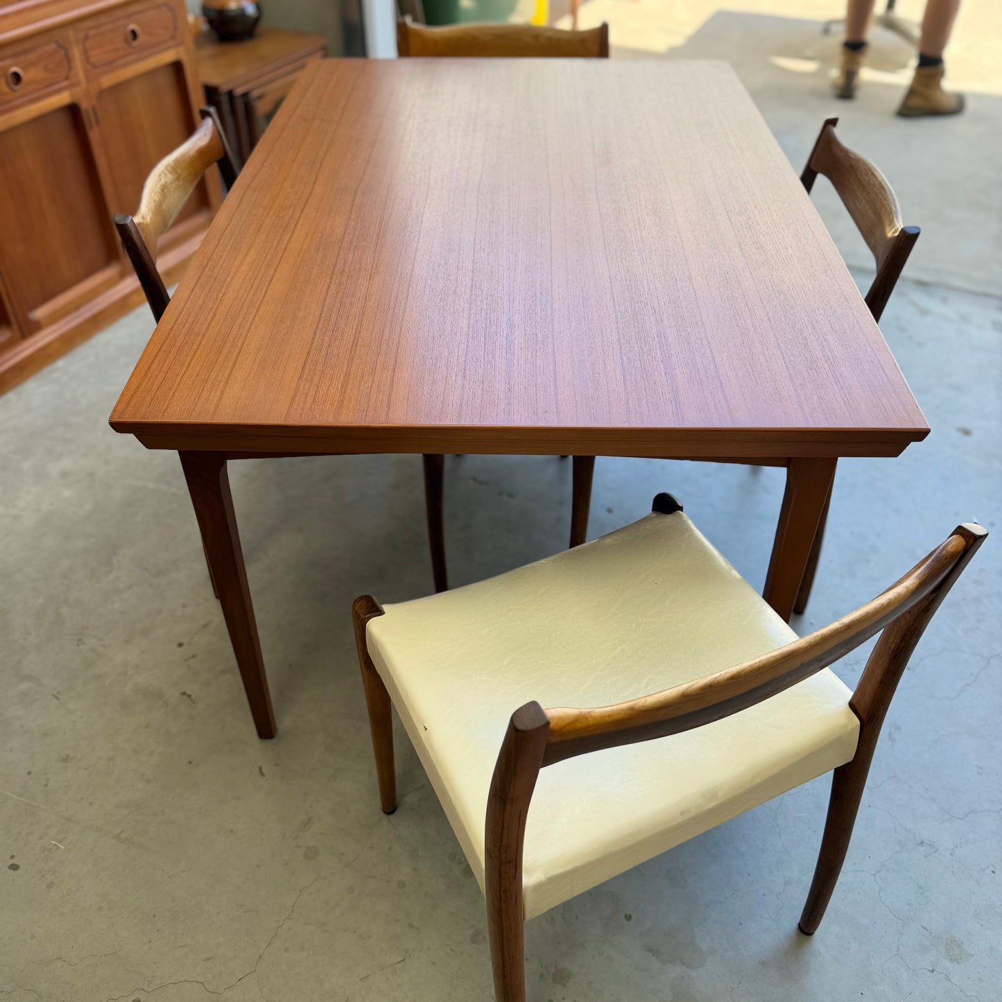 The Fler 64 Rectangular extension Table (Refine) is paired with three wooden chairs—one with a white cushion seat—set on a concrete floor, with more wooden furniture visible in the background.