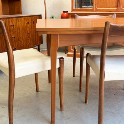 A Fler 64 Rectangular Extension Table (Refine) with matching chairs and white cushions sits on a concrete floor, surrounded by mid-century modern wooden cabinets and a red vase, highlighting vintage Australian design.