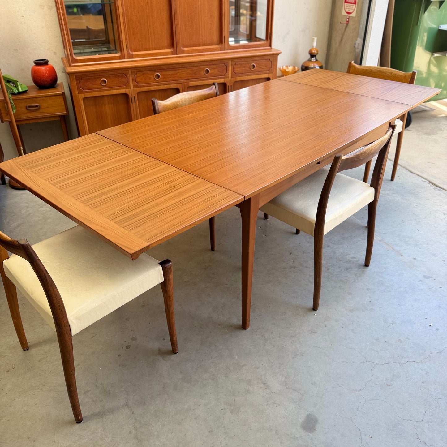 A Fler 64 Rectangular extension Table (Refine), a mid-century modern dining table with leaf extensions, is paired with four matching light-upholstered chairs in a room showcasing vintage Australian design elements.