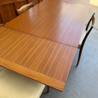 A Fler 64 Rectangular Extension Table (Refine) with a smooth, striped grain is surrounded by chairs with light-colored seat cushions, creating a vintage Australian look on a light floor indoors.