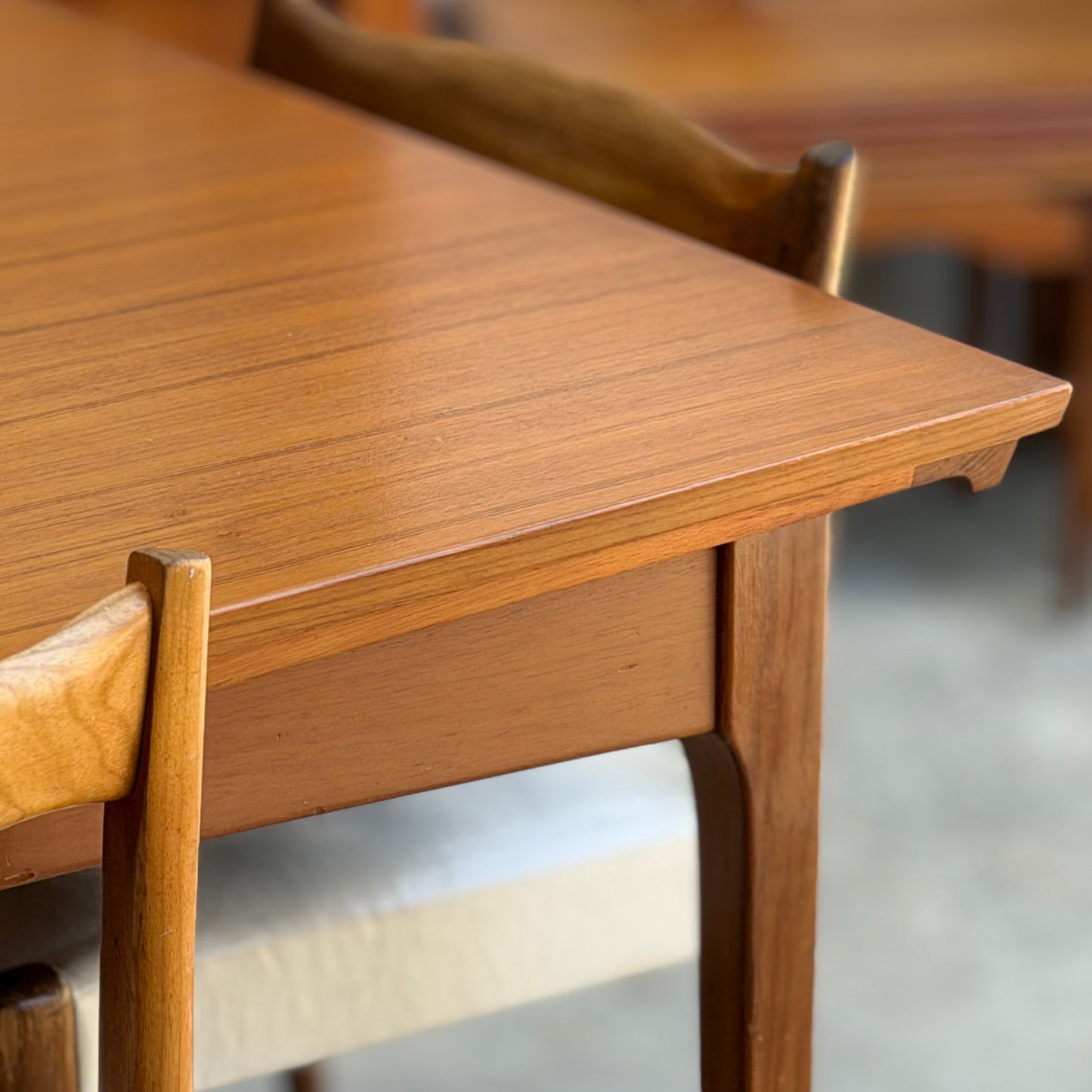 Close-up of the Fler 64 Rectangular Extension Table (Refine), inspired by vintage Australian design, showcasing its smooth grain, angled edges, and matching chairs with curved backs and light cushioned seats.