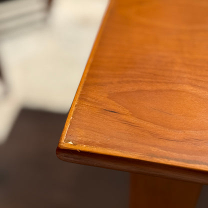 A close-up of the Mid Century Teak Danish Style Coffee Table – Circa 1970s (Revive) shows a small dent and scratch on its warm brown, teak-finished corner. The classic style stands out against a softly blurred background.