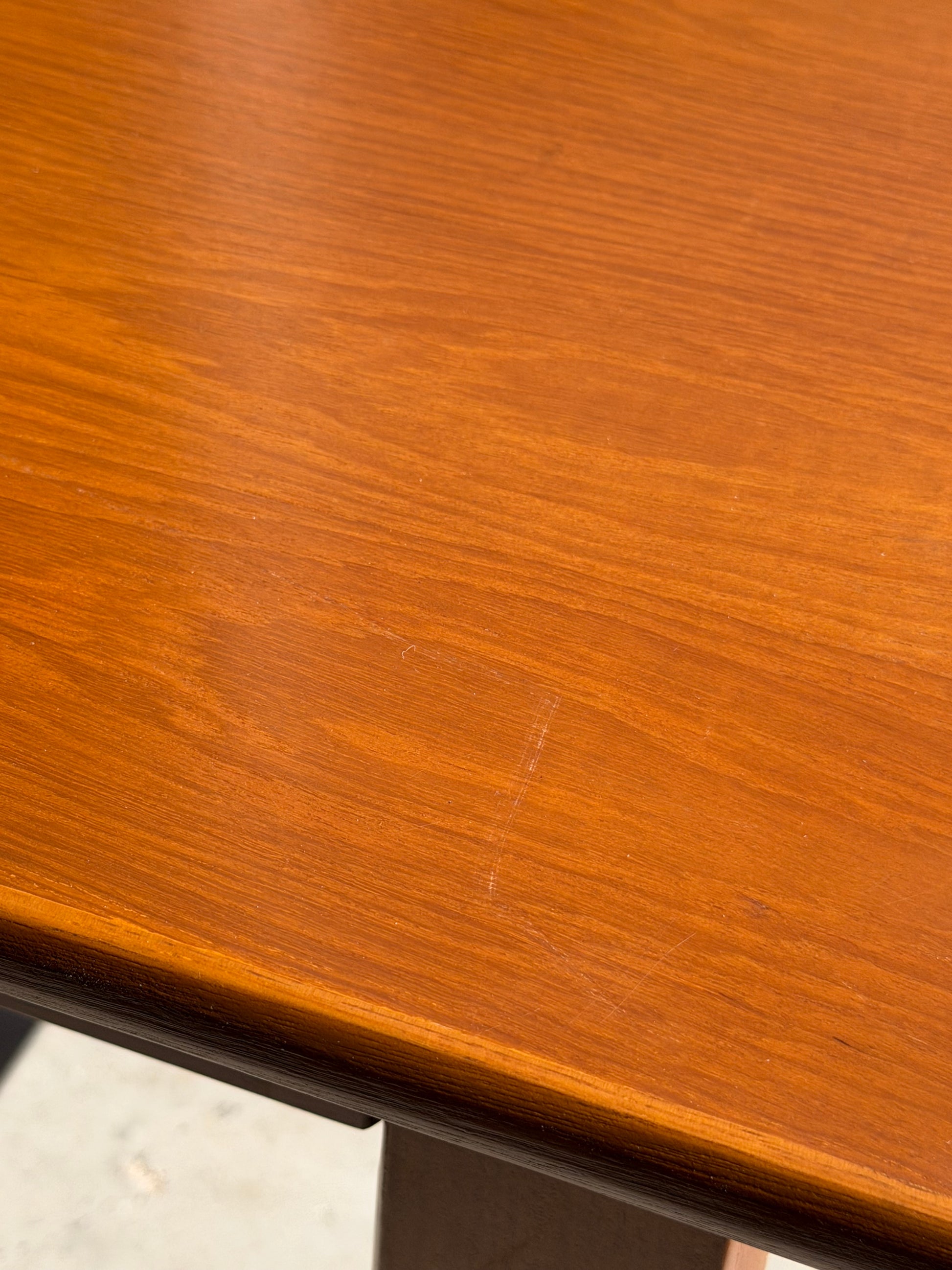A close-up of the Mid Century Teak Danish Style Coffee Table – Circa 1970s (Revive), featuring a warm brown finish, visible wood grain, and a subtle scratch. Sunlight enhances the vintage Scandinavian charm and texture of this classic piece.