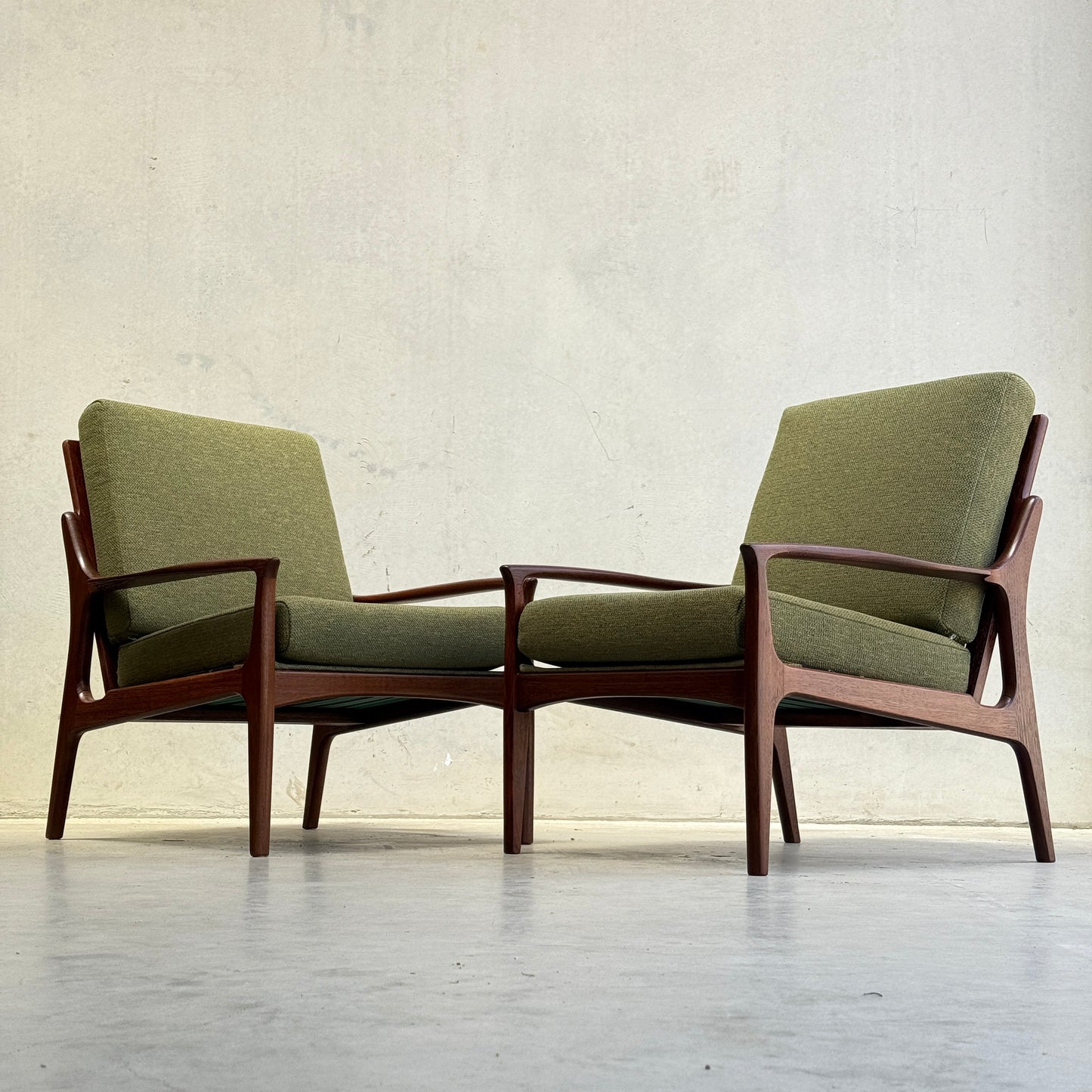 Two Don Rex Armchair - Green Forest (Rediscover) pieces, with green cushions and wooden frames, sit side by side on a light floor against a plain, light-colored wall, representing mid-century Australian furniture design.