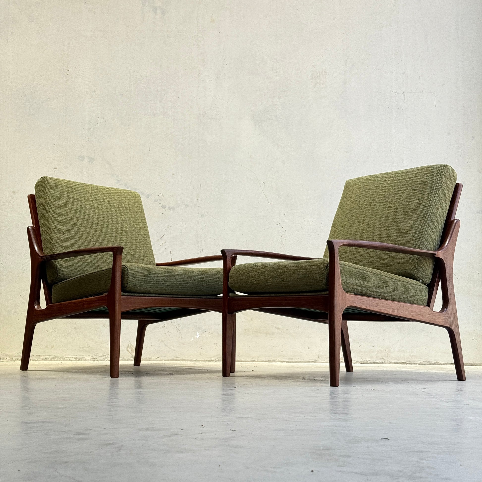 Two Don Rex Armchair - Green Forest (Rediscover) pieces, with green cushions and wooden frames, sit side by side on a light floor against a plain, light-colored wall, representing mid-century Australian furniture design.