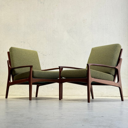 Two Don Rex Armchair - Green Forest (Rediscover) pieces, with green cushions and wooden frames, sit side by side on a light floor against a plain, light-colored wall, representing mid-century Australian furniture design.