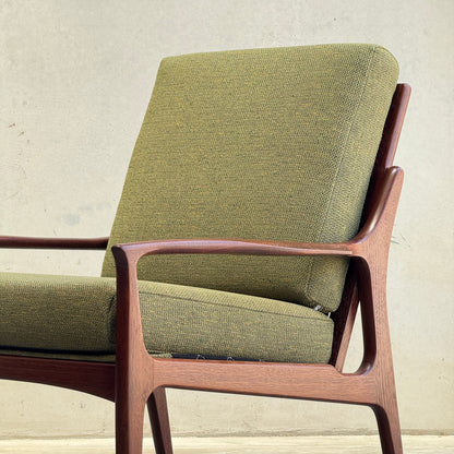 The Don Rex Armchair - Green Forest (Rediscover) features green upholstered cushions and a wooden frame, showcasing clean lines and minimalist Danish modernism against a light backdrop.