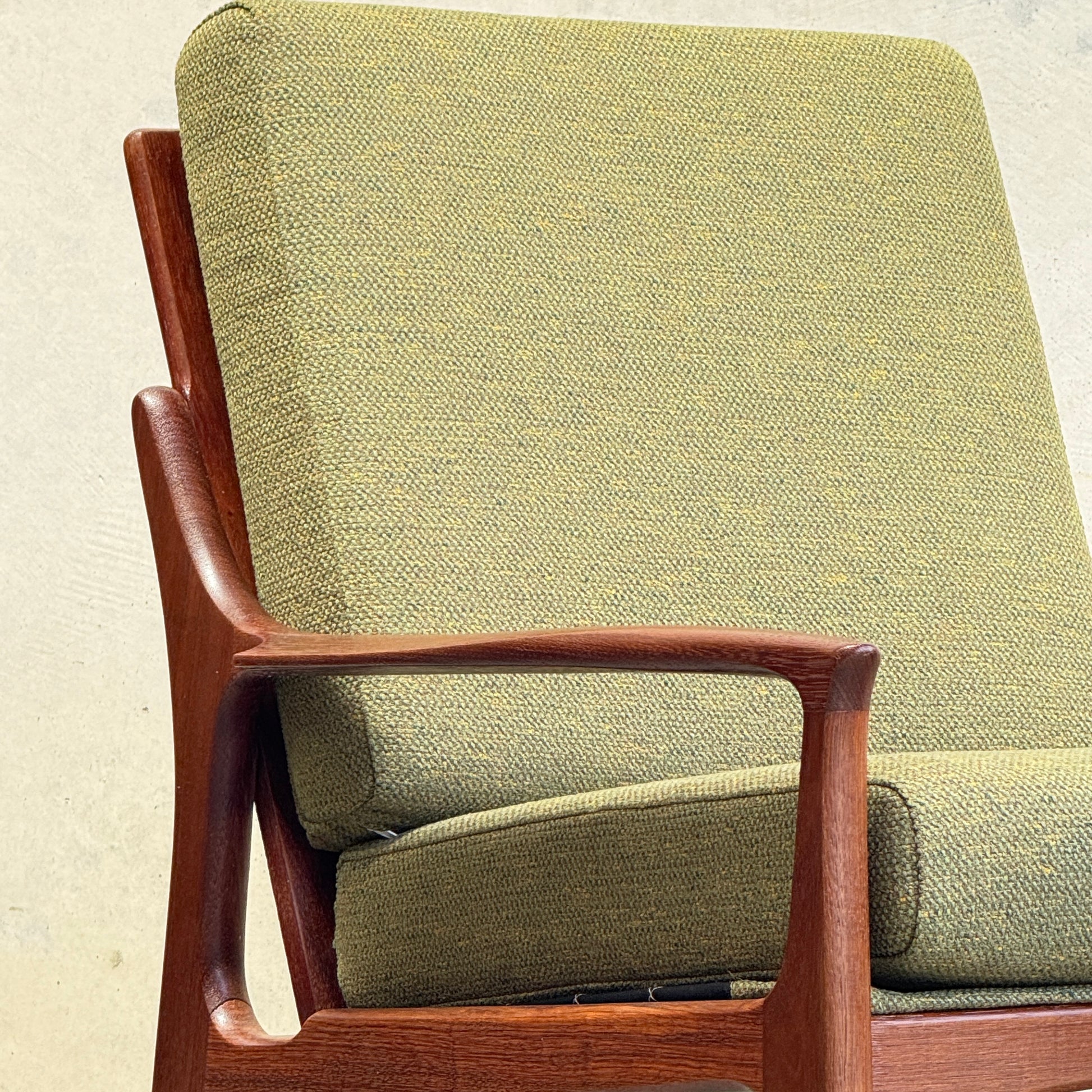 Close-up of the Don Rex Armchair - Green Forest (Rediscover): a mid-century Australian classic with textured green cushions, wooden frame, and Danish modern-inspired armrest and backrest, set against a neutral background.