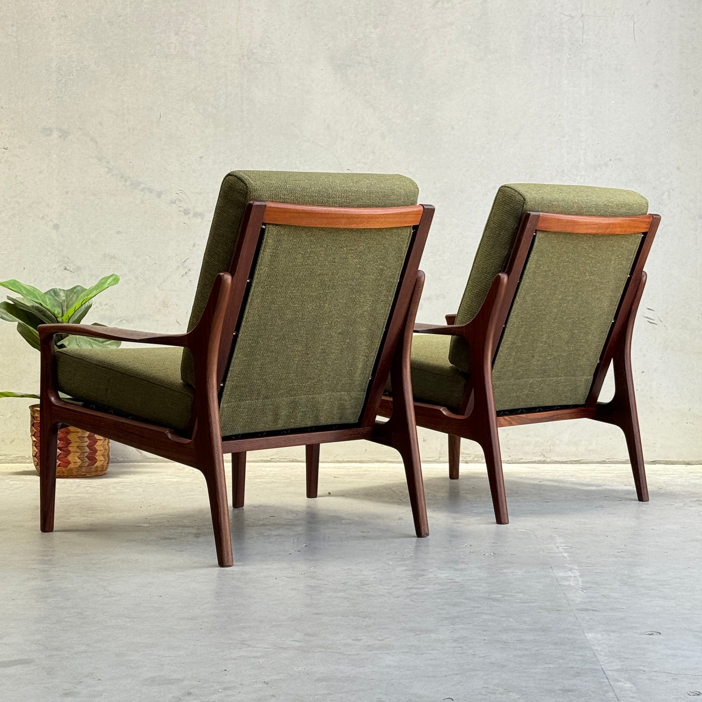 Two Don Rex Armchair - Green Forest (Rediscover) with wooden frames and green cushions sit on a light floor beside a small potted plant, showcasing mid-century Australian elegance against a plain light-colored wall.