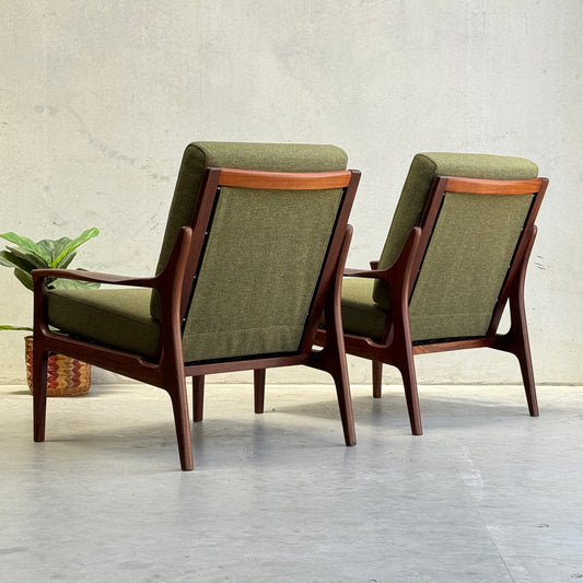 Two Don Rex Armchair - Green Forest (Rediscover) with wooden frames and green cushions sit on a light floor beside a small potted plant, showcasing mid-century Australian elegance against a plain light-colored wall.