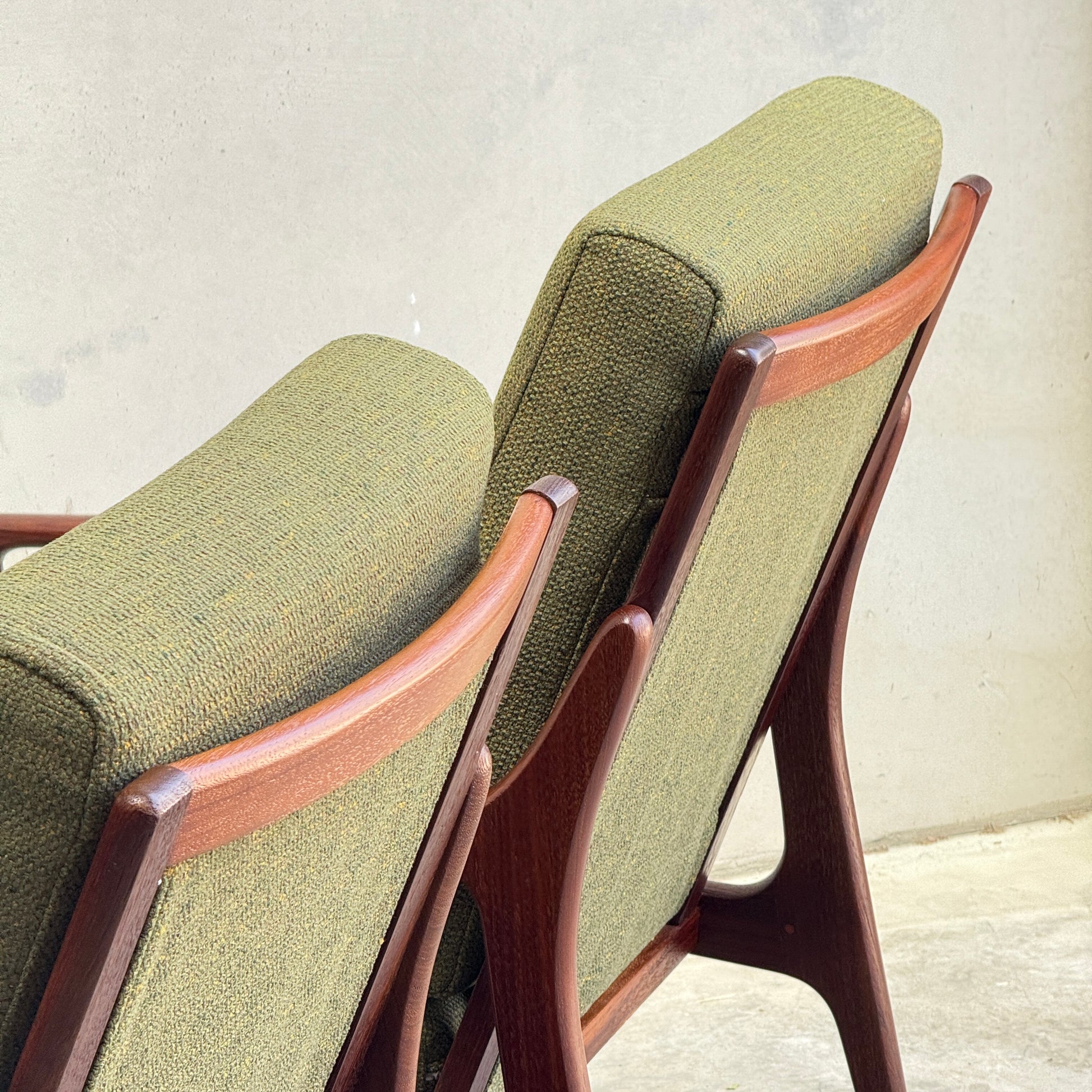 Two Don Rex Armchair - Green Forest (Rediscover) chairs with green cushions and wooden frames sit side by side, backs to the camera, against a light wall and concrete floor—showcasing classic mid-century Australian furniture design.