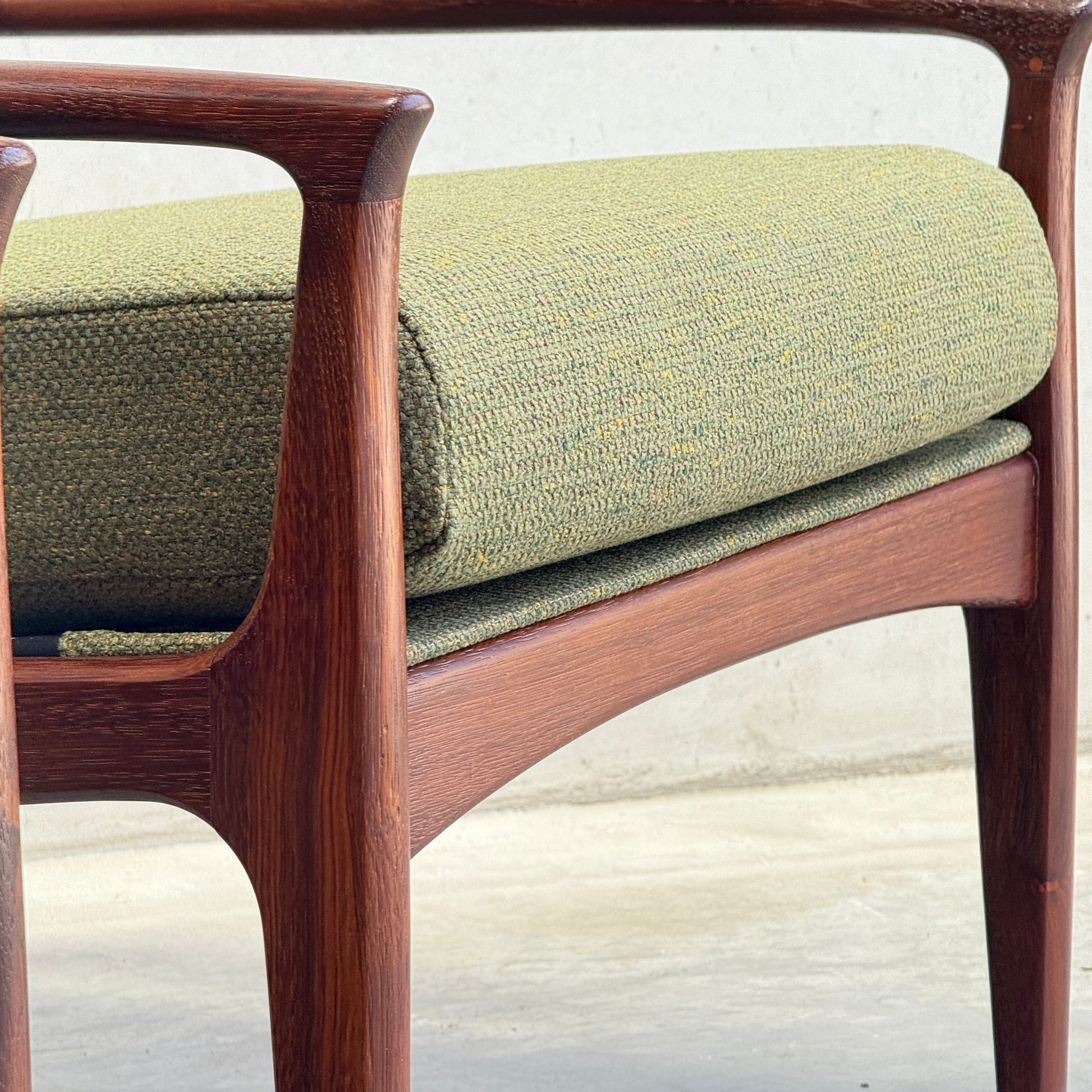 Close-up of the Don Rex Armchair - Green Forest (Rediscover), a mid-century modern wooden chair with curved armrests and green textured upholstery, inspired by Danish modernism, set against a neutral background.