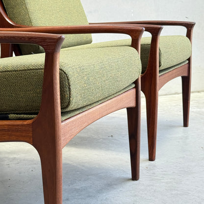 Close-up of two Don Rex Armchair - Green Forest (Rediscover), featuring wooden frames and green cushions, showcasing Danish modernism on a smooth, light floor against a plain wall.