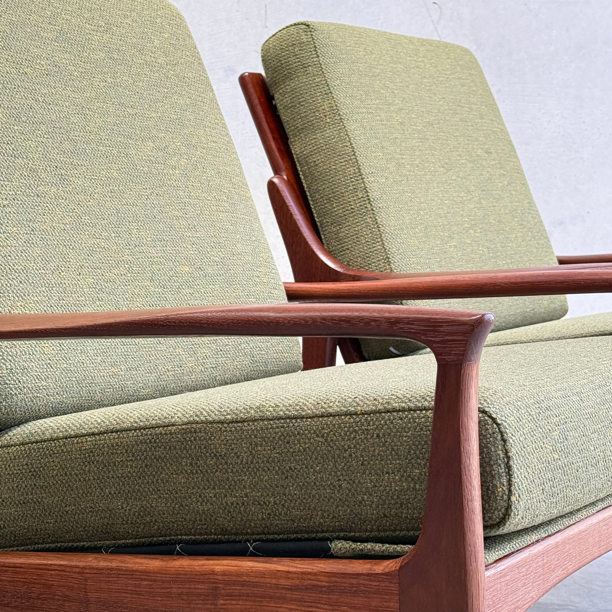 Close-up of two Don Rex Armchair - Green Forest (Rediscover) with wooden frames and green cushions, side by side against a light wall—a refined example of mid-century Australian furniture inspired by Danish modernism.