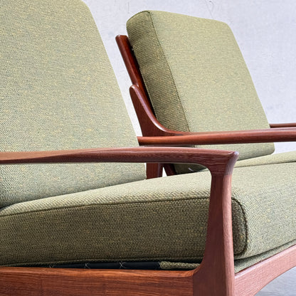 Close-up of two Don Rex Armchair - Green Forest (Rediscover) with wooden frames and green cushions, side by side against a light wall—a refined example of mid-century Australian furniture inspired by Danish modernism.