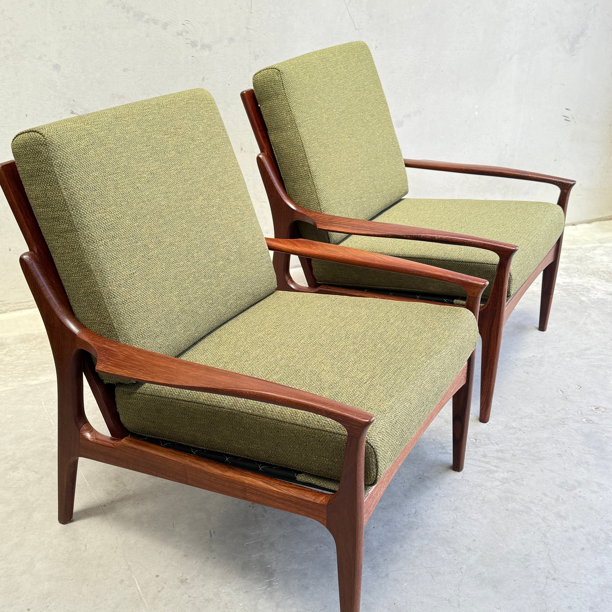 Two Don Rex Armchair - Green Forest (Rediscover) seats with green upholstery and wooden frames sit side by side on a light gray floor against a plain, light-colored wall.