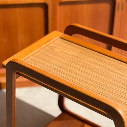 A close-up of the Mid-Century Noblett Drinks Trolley with removable tray and original castors, showcasing its clean lines and smooth light wood grain finish in a sunlit room, positioned near matching Noblett furniture.
