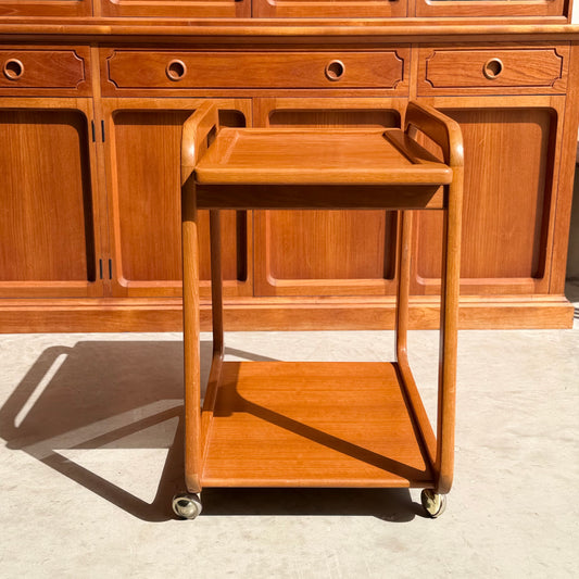 The Mid-Century Noblett Drinks Trolley – Removable Tray & Original Castors (Revive) sits before a matching cabinet, sunlight streaming in and casting gentle shadows on the floor.