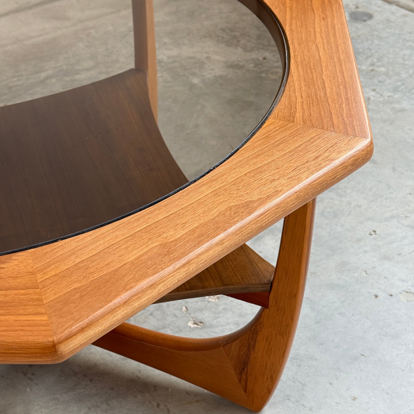 Close-up of the Octagonal Mid Century Coffee Table by Kalmar Furniture, featuring a hardwood frame, smoked glass top, and integrated magazine rack. Its warm finish and rounded edges highlight Australian design on a concrete floor.