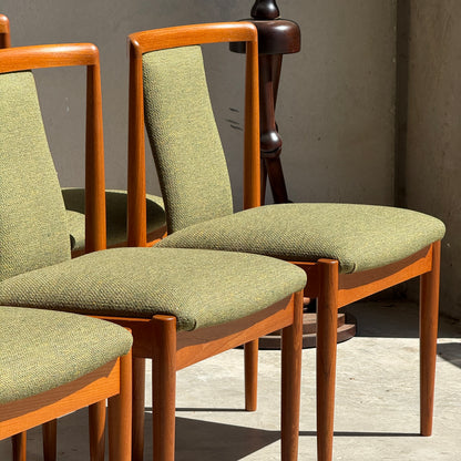Six fully restored Parker T-Back Number 88 dining chairs in forest green upholstery are bathed in sunlight, creating shadows on a concrete floor. The timeless set from Rediscover stands out against a beige wall.