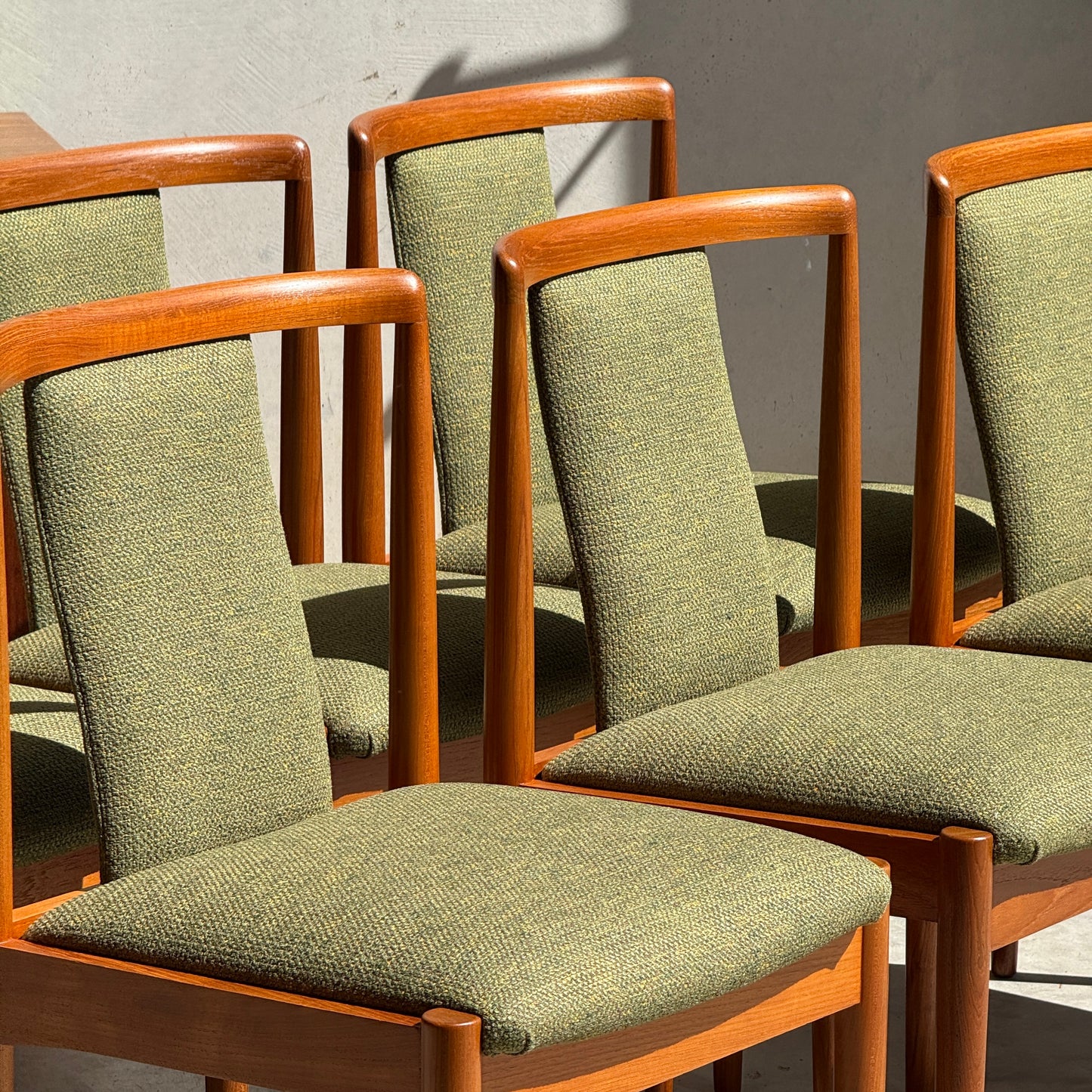 Six fully restored Parker T-Back Number 88 dining chairs in forest green from Rediscover are arranged in bright sunlight, casting bold shadows on a plain light-colored wall.