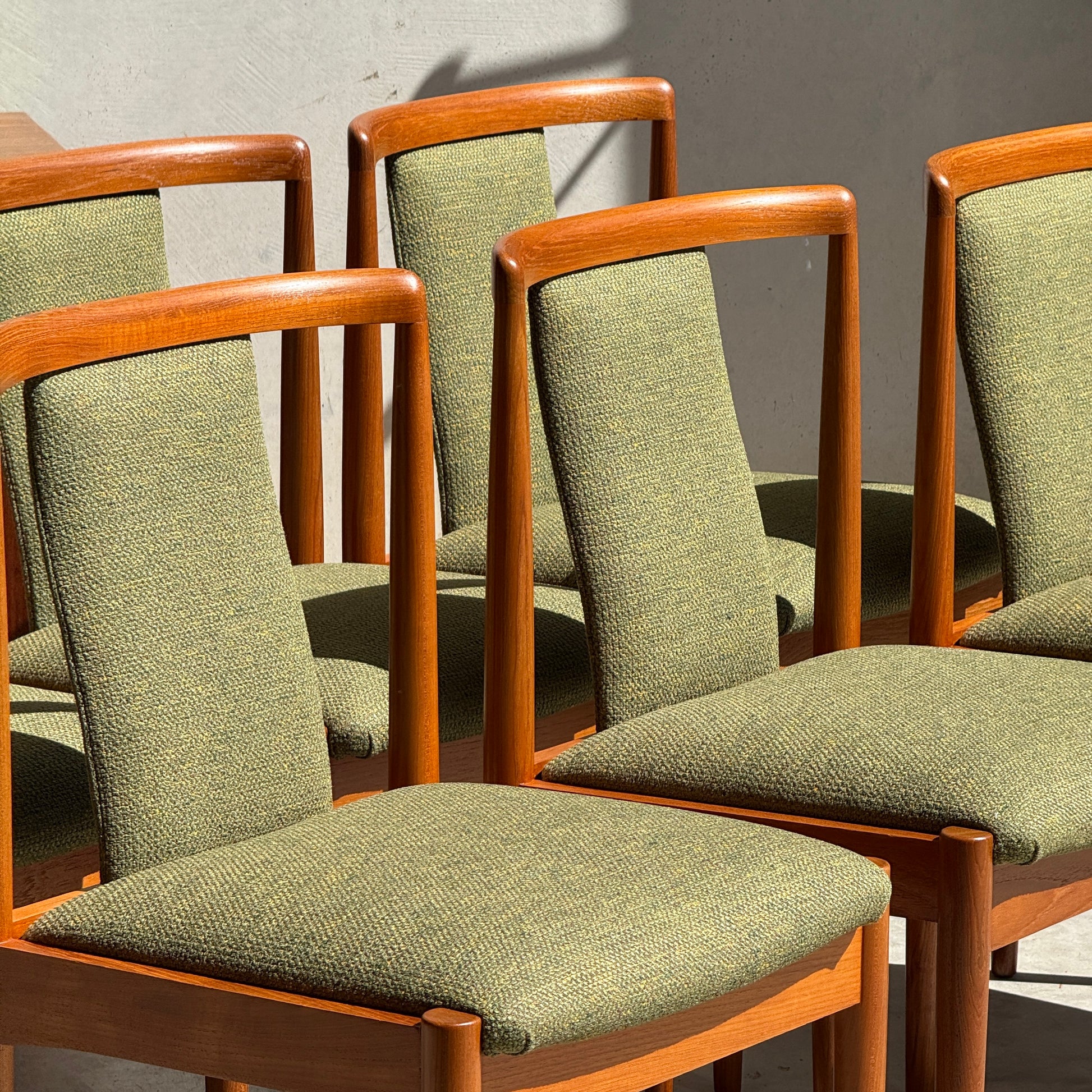 Six fully restored Parker T-Back Number 88 dining chairs in forest green from Rediscover are arranged in bright sunlight, casting bold shadows on a plain light-colored wall.