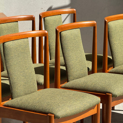 Six fully restored Parker T-Back Number 88 dining chairs in forest green from Rediscover are arranged in bright sunlight, casting bold shadows on a plain light-colored wall.