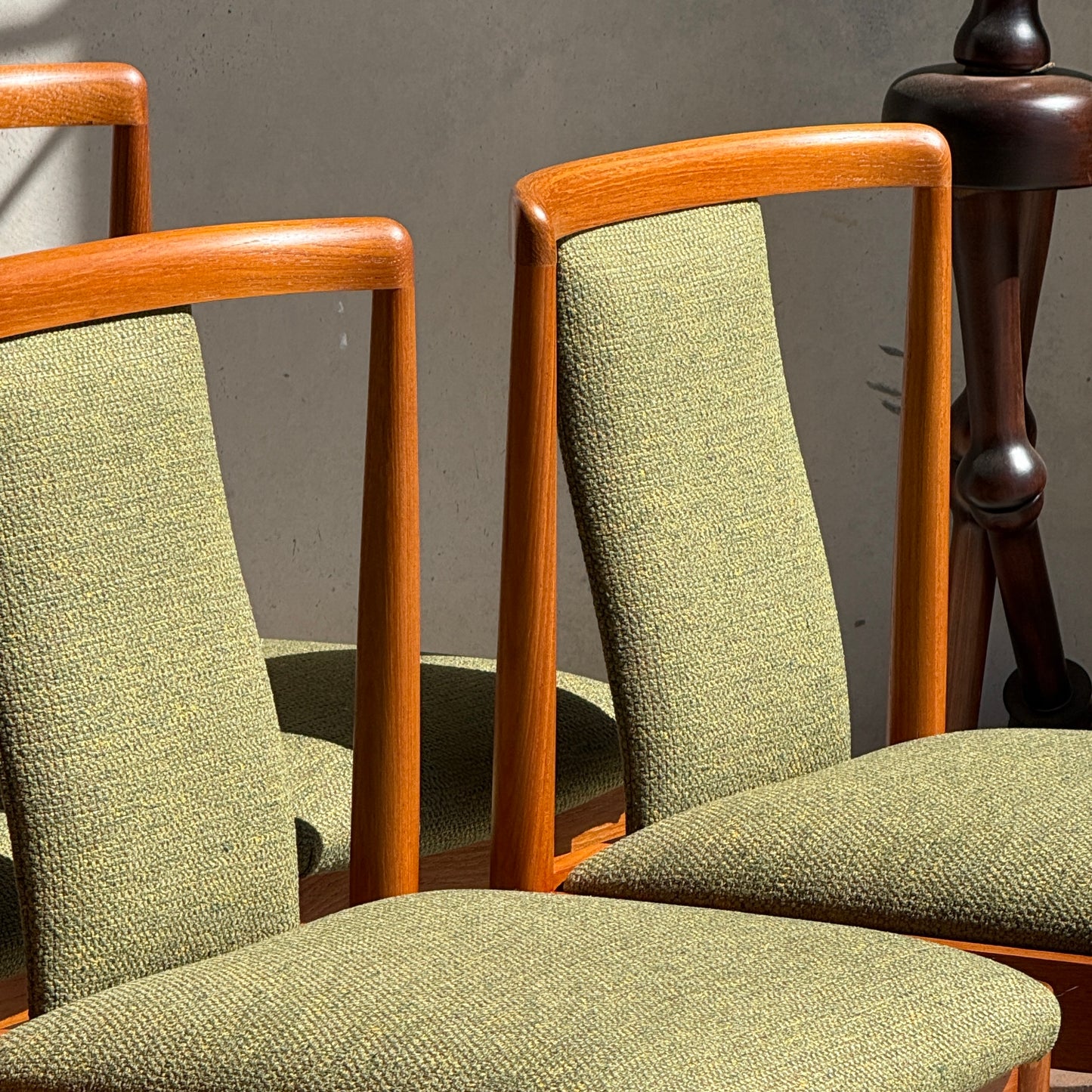 Two fully restored Parker T-Back Number 88 dining chairs in forest green from a set of 6 (Rediscover) are placed next to a dark wooden side table, all set against a neutral gray wall with bright sunlight.