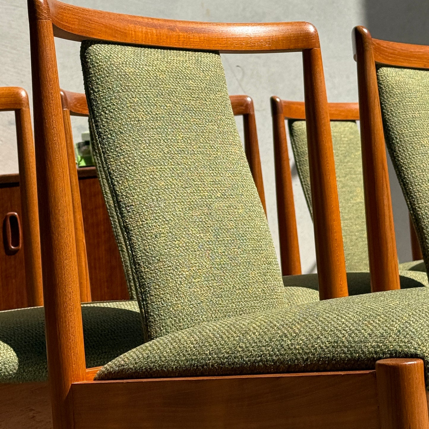 Close-up of the Fully Restored Parker T-Back Number 88 Dining Chairs Set of 6 - Forest Green (Rediscover), arranged in a row with sunlit, textured upholstery and a mid-century sideboard visible in the background.